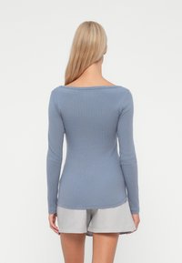 Cămășuță cu mânecă lungă dintr-un material ribat de culoare albastră deschisă, cu gât larg și croială ajustată, asociată cu pantaloni scurți gri. Finisaj texturat și senzație moale.