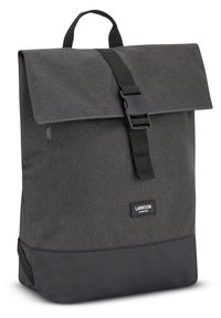 Mochila de tela gris con solapa plegable, correa ajustable y sección inferior negra. Presenta un parche con logo cerca de la base.