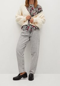 Cardigan lavorato a maglia beige, blouse floreale rossa e nera, jeans grigi a vita alta, mocassini neri. Tessuto texture e vestibilità rilassata.