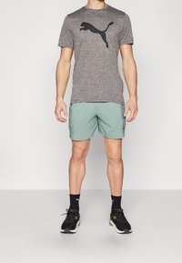 Šedé sportovní tričko s černým logem, doplněné světle zelenými šortkami. Černé tenisky se zelenými akcenty dokončují celý outfit.