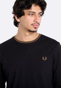 Zwarte lange mouwen t-shirt van katoen, met een ronde hals en bruine streepdetails, en een klein geborduurd logo op de linkerkant van de borst.