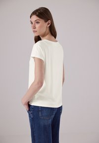 Lys cremefarvet kortærmet top med en rund halsudskæring, parret med mørkeblå denimjeans. Stoffet ser blødt ud med en glat tekstur.