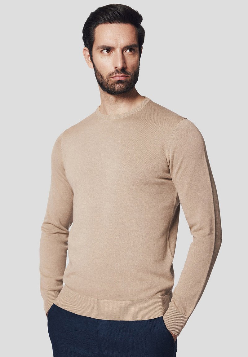 Beżowy sweter z okrągłym dekoltem, z długimi rękawami, ściągaczami u rękawów i u dołu, wykonany z miękkiego materiału, z gładką fakturą i dopasowanym krojem.