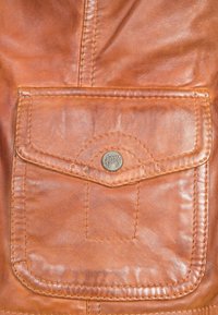 Zak van een leren jas in kastanjebruin met gestikte randen, voorzien van een metalen logoknop. Soepele textuur met zichtbare nerfpatronen.