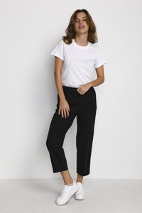 T-shirt blanche à manches courtes associée à un pantalon noir court et des baskets blanches. Le pantalon a une coupe droite et une texture lisse.