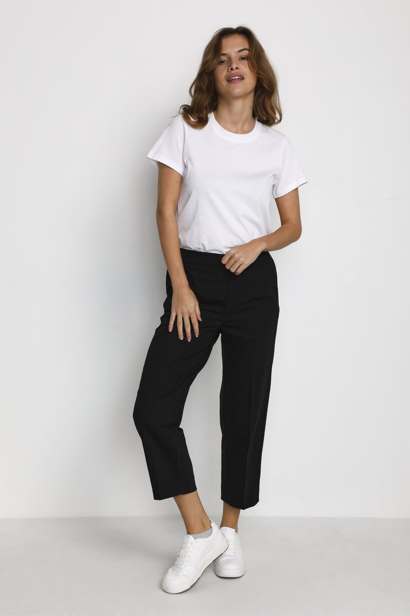 T-shirt blanche à manches courtes associée à un pantalon noir court et des baskets blanches. Le pantalon a une coupe droite et une texture lisse.