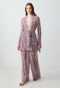 Ensemble en tissu transparent à imprimé léopard comprenant une longue veste ceinturée et un pantalon ample dans des tons de rose et de marron. Texture lisse, design décontracté.