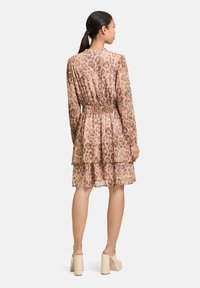 Leopardenmuster Kleid aus transparenter Stoff, mit einem gerafften Taillenbereich, langen Ärmeln und mehrlagigem Rüschensaum, ergänzt durch beigefarbene Blockabsatzschuhe.