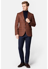 Brązowa marynarka w kratę z wykrojem w szpic, pojedynczym zapięciem na guzik, granatowy golf, granatowe spodnie i brązowe botki za kostkę. Strukturalny krój.