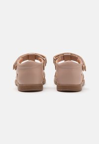 Vaaleanpunaiset sandaalit, joissa on säädettävät hihnat, sileä nahkatekstuuri ja ruskea kumipohja. Avoimet takat ja minimalistinen muotoilu.