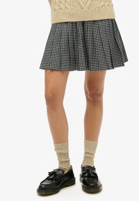 Rutet plisseret nederdel i marineblå og creme, parret med beige ribbede strømper og sorte læder loafers med sløjfedetaljer.