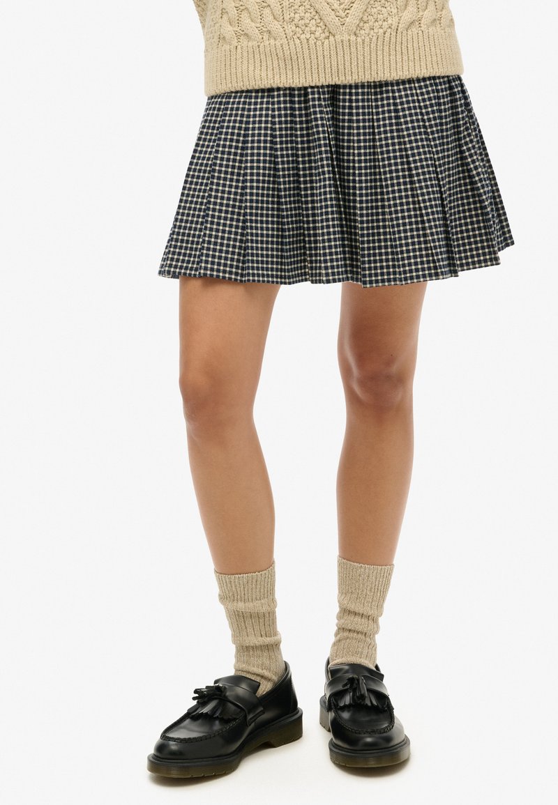 Minifalda de cuadros plisada en azul marino y crema, combinada con medias de punto beige y mocasines de cuero negro con detalles de lazo.