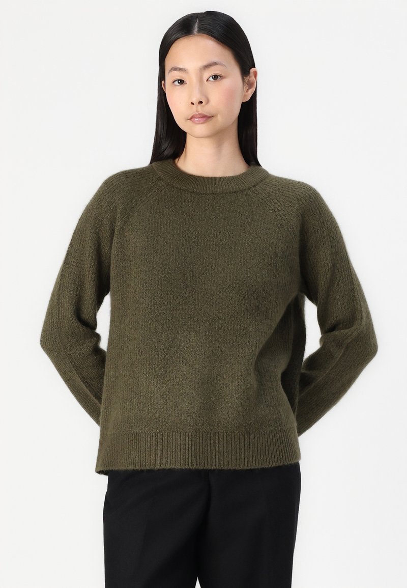 Maglione a maglia verde oliva con scollo rotondo, maniche lunghe e vestibilità morbida. Tessuto morbido e dettaglio a coste sull'orlo. Abbinato a pantaloni scuri.
