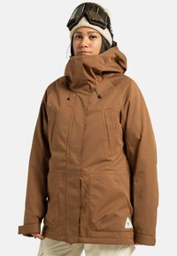 Braune, isolierte Jacke mit hohem Kragen, verstellbarer Kapuze, zwei vorderen Taschen und elastischen Bündchen. Verfügt über einen kleinen Logo-Patch am Saum.