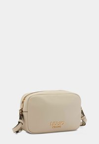 Beige faux læder crossbody taske med rektangulær form, guldfarvet hardware, lynlåslukning og præget brandlogo på fronten.