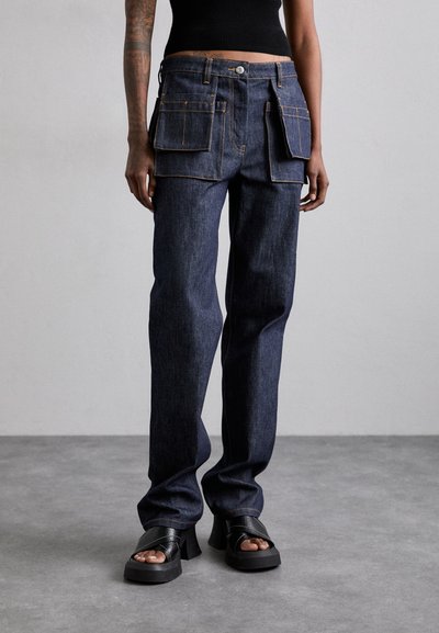Mørkeblå denim cargo bukser med to store frontlommer og orange syninger. Lige ben-design og båret med sorte blokhælede sandaler.