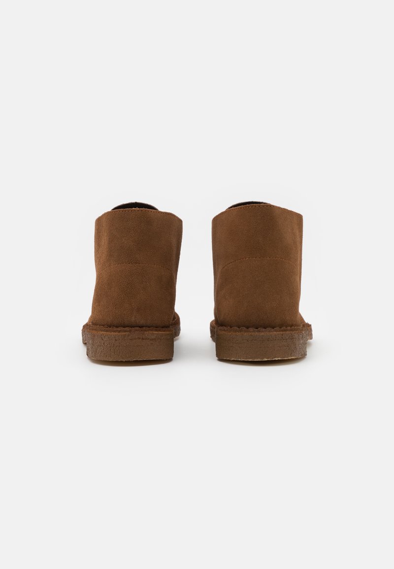Botas de tobillo de ante marrón con textura suave, forma redondeada y suela de goma marrón. Sin herrajes o patrones visibles.
