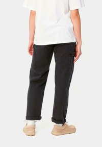 Pantalones cargo negros con bolsillos laterales, tobillos ajustados y un corte holgado, combinados con zapatillas beige y calcetines blancos. La camiseta es blanca y de corte holgado.