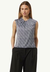 Marineblauwe mouwloze blouse met een geplooide halslijn en een geometrisch patroon in het wit. Glad stof; gecombineerd met zwarte broek.