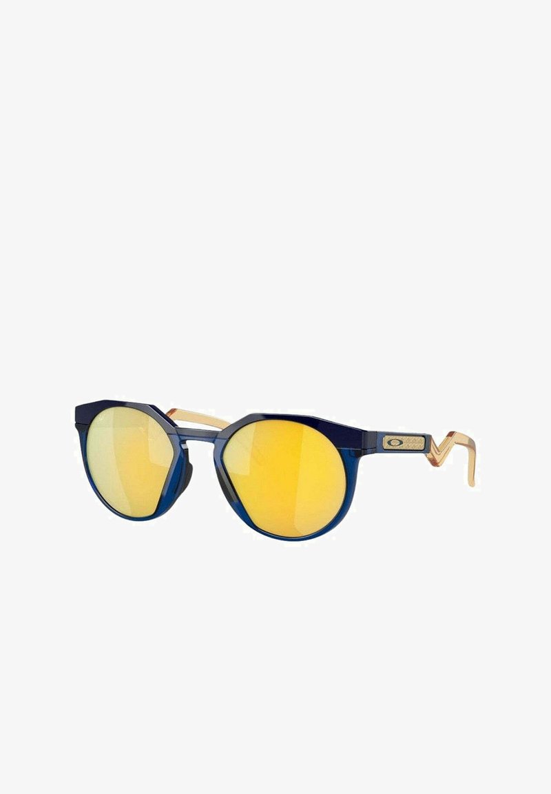 Niebieskie okulary przeciwsłoneczne z okrągłymi soczewkami, z żółtym lustrzanym wykończeniem. Plastikowa oprawka z złotymi akcentami na zausznikach i unikalnym, kanciastym designem.