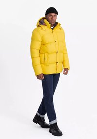 Gul pufferjakke med hætte, med et ternet for. Slim fit jeans og sorte snørrebåndsstøvler fuldender outfittet.