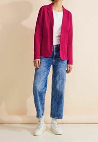 Blazer fuchsia avec deux poches avant, associé à un t-shirt blanc et un jean bleu ample, porté avec des baskets blanches. Texture lisse.