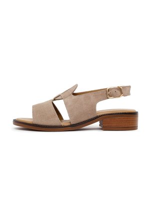 Beige suede open-toe slingback sandal with cutout sides, gold buckle strap, and low stacked wooden heel.