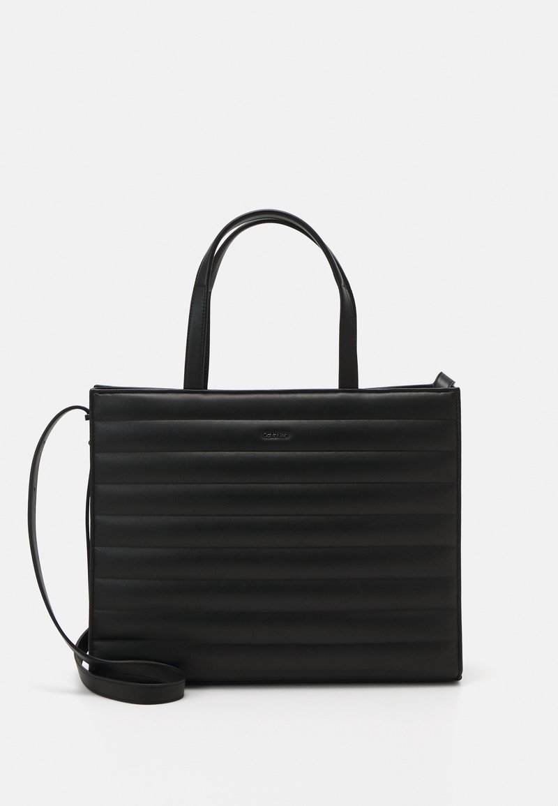 Sac à main rectangulaire noir avec matelassage horizontal, deux poignées supérieures et une longue bandoulière réglable sur un fond clair.