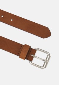 Ceinture en cuir brun avec une texture lisse, boucle en métal argenté et une extrémité effilée. Présente plusieurs trous d'ajustement et un bord cousu.