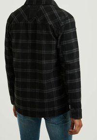 Black and gray plaid flannel shirt with a buttoned cuff, featuring a straight hem and a distinct yoke design on the upper back.