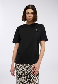 T-shirt nera in cotone a maniche corte, con un piccolo logo ricamato a forma di bicchiere da cocktail sul petto. Abbinato a una gonna a stampa leopardata.