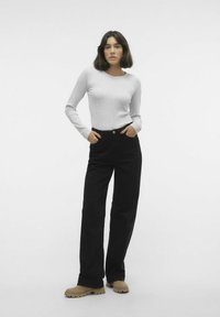 Maglietta grigia a maniche lunghe abbinata a pantaloni neri a vita alta e a gamba larga, con scarpe beige a suola testurizzata. Outfit semplice e casual.