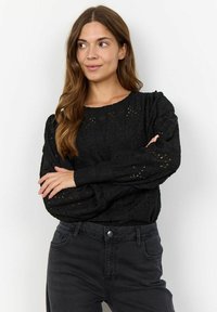 Black textured sweater with puffed sleeves, featuring lace-like openwork details. Paired with dark jeans, the outfit has a casual look.