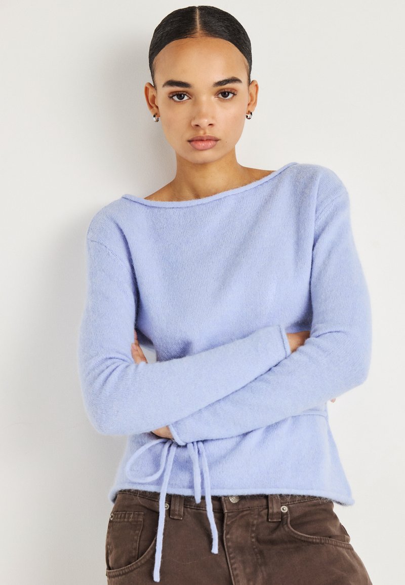 Pull en maille bleu clair avec un large décolleté, manches longues et un ourlet à cordon de serrage. Texture douce, coupe décontractée et détails minimalistes.
