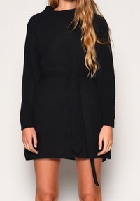 Schwarzes Strickkleid mit langen Ärmeln, strukturiertem Finish und gebundenem Taillengürtel. Verfügt über einen hohen Ausschnitt und einen leicht lockeren Schnitt.