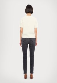 Helles cremefarbenes, geripptes Strickoberteil mit kurzen Ärmeln, kombiniert mit dunkelgrauen Slim-Fit-Jeans. Das Outfit hat ein minimalistisches Design und wird mit beigefarbenen Blockabsatzschuhen ergänzt.