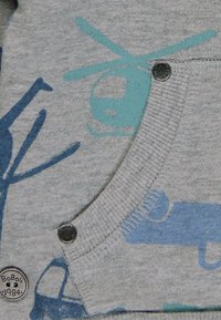 Tela gris con patrones de helicópteros y armas en azul y verde azulado, con un cuello acanalado y dos botones decorativos en el costado.