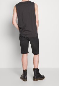 Person wearing black sleeveless shirt, black knee-length shorts, black socks, and black lace-up boots, standing against a plain white background.