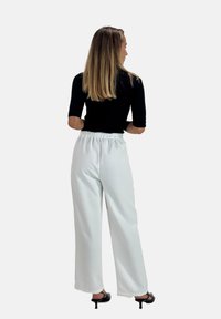 Witte wijde broek met een elastische tailleband, gecombineerd met een zwarte aansluitende top. De stof lijkt soepel en licht, geschikt voor casual draag.