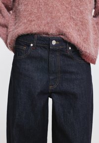 Sötétkék farmernadrág sima textúrával, kontrasztos varrással, ötpocketes kialakítással és ezüstszínű gombos záródással.