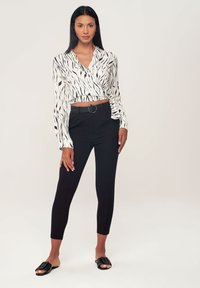 Blusa avvolgente a righe bianche e nere, design cropped con nodo laterale, abbinata a pantaloni neri a vita alta e sandali neri piatti.