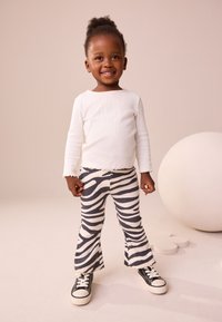 Hvid, ribbet, langærmet top kombineret med sorte og hvide stribede, udvidede leggings og sorte lærredssneakers. Bløde teksturer, afslappet stil.