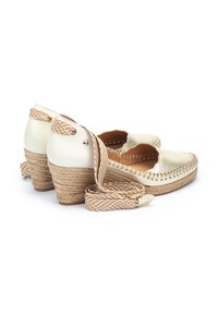 Chaussures à talons compensés crème avec un dessus texturé, un talon enveloppé de jute et des liens en tissu tressé au niveau de la cheville. Présente des bords festonnés et des détails en métal doré.