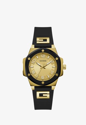 Reloj dorado con correa de silicona negra. Presenta números grandes y claros, una esfera dorada texturizada y un distintivo logo de 'G' en la correa.
