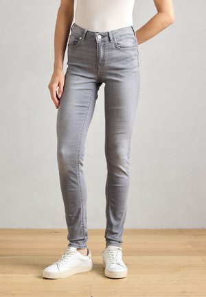 Grå skinny jeans med høy midje, fem lommer, beltehaller og et subtilt stretch-stoff, kombinert med hvite joggesko.