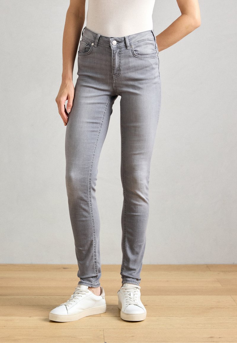 Grå skinny jeans med høy midje, fem lommer, beltehaller og et subtilt stretch-stoff, kombinert med hvite joggesko.