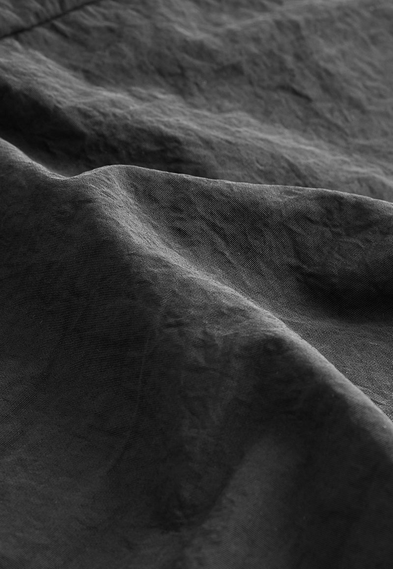 Tissu gris foncé avec une surface texturée, affichant de doux plis et un léger éclat, évoquant une apparence riche et drapée.