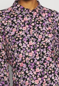 Květinová košile vyrobená z lehkého materiálu, s černým pozadím a růžovými, fialovými a bílými květy, a klasickým designem límce.