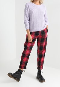 Ljuslila stickad tröja med ribbad textur, kombinerad med röd och svart rutiga byxor. Avslutad med svarta snörade ankelstövlar.