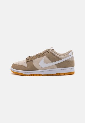 Nike Low-Top Sneaker in beige und hellbraunem Veloursleder mit weißem Nike-Swoosh und Gummisohle, von der Außenseite auf weißem Hintergrund gezeigt.